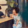 lifestyle image of a woman leaning on a bar-style table beside a couple other people talking